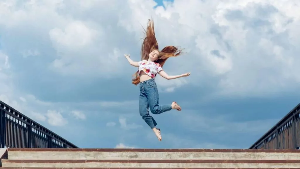 Young teen girl jumping up on the blue cloudy sky background