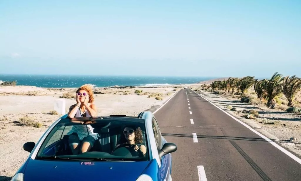 convertible car and couple of adult female friends have fun together driving on a long road