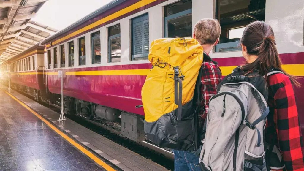 Two backpackers at a train station boarding a red and yellow train