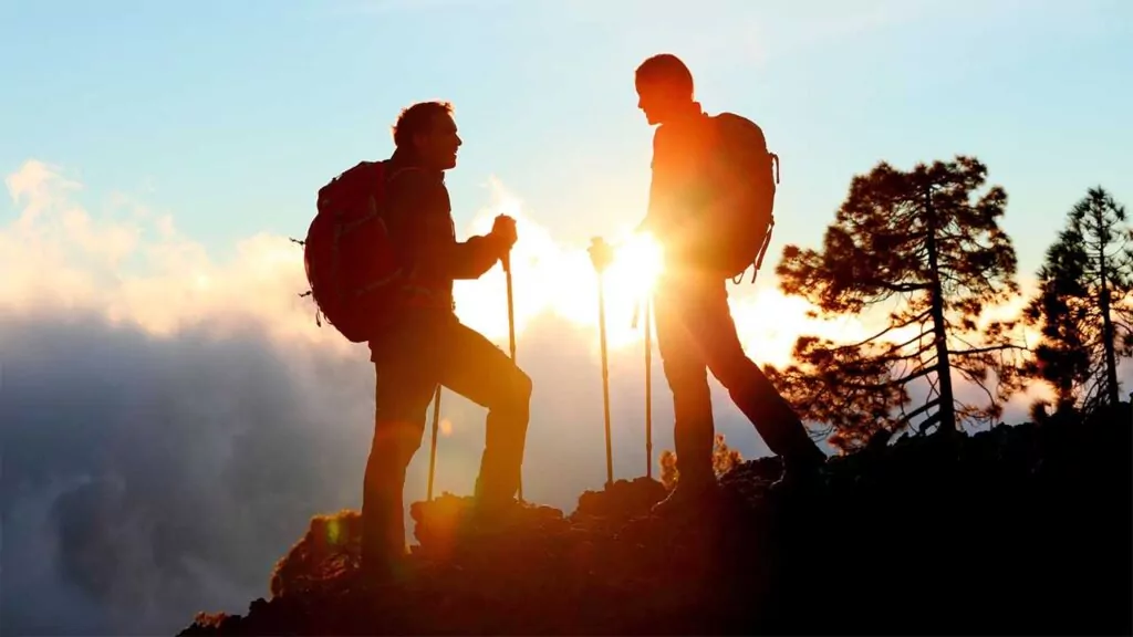 Silhouette of two hikers at sunset on a mountain trail.