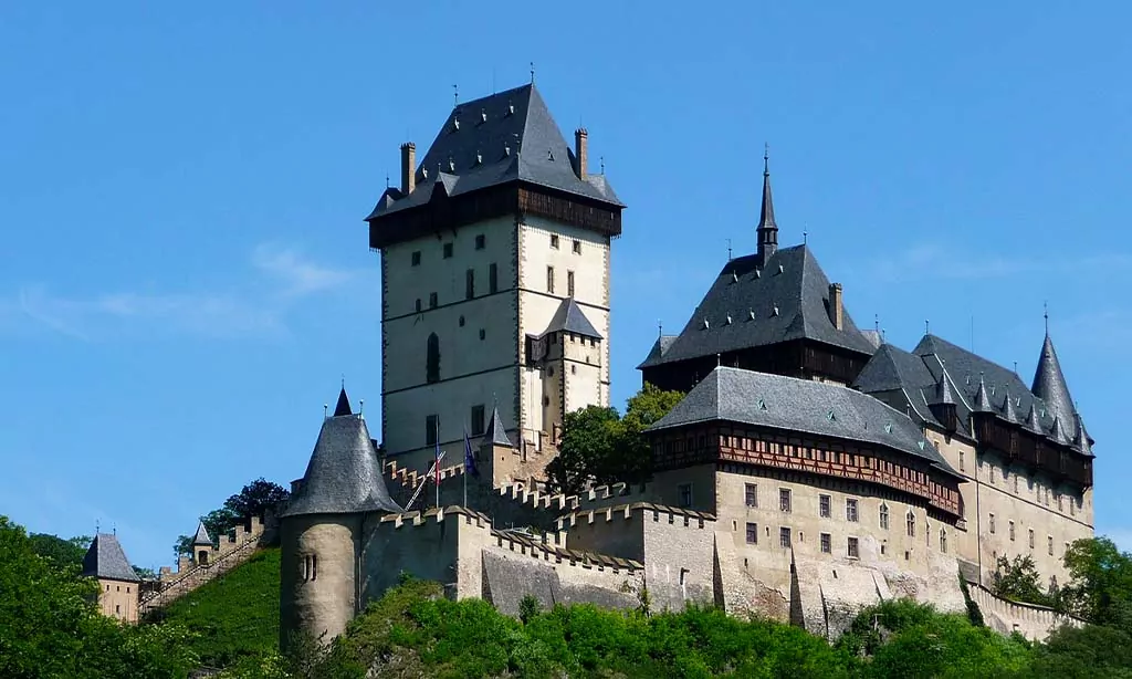 Historic castle on a hilltop, with towers and fortified walls, against a clear blue sky.