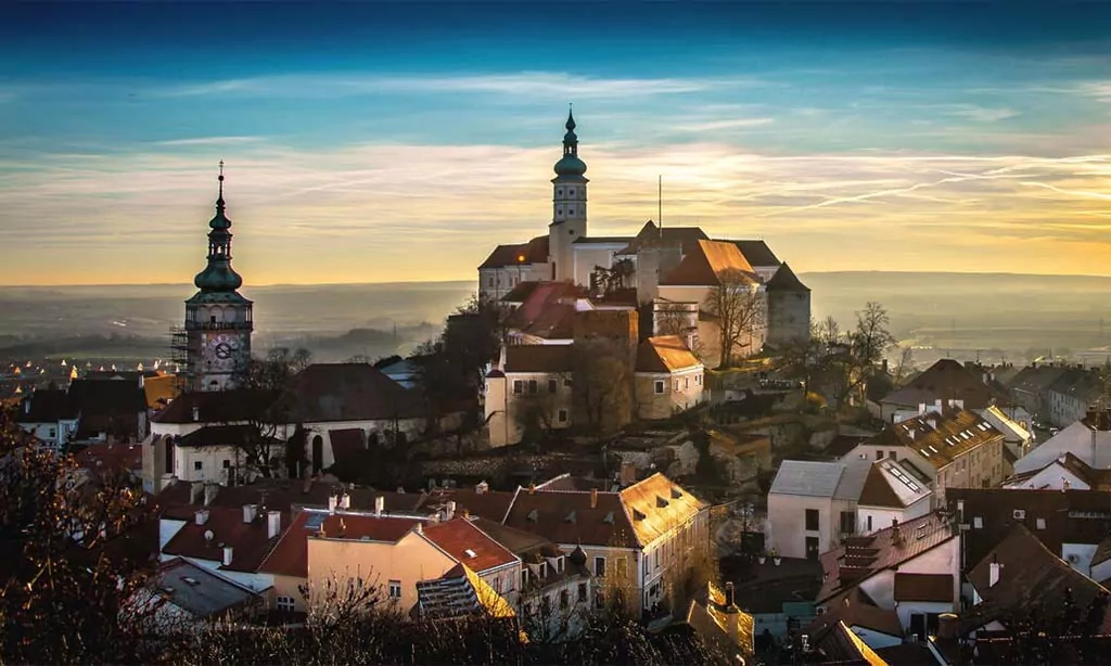 Historic hilltop castle and clock tower at sunset, scenic town with old-world charm and picturesque views.